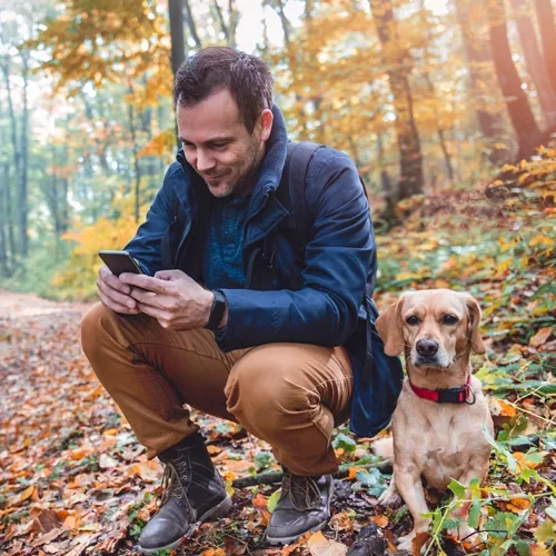 guy on the phone alongside his dog in the forest